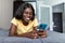 Smiling portrait of african american female laying relaxing on home bed holding smart phone, networking in indoors bedroom