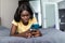 Smiling portrait of african american female laying relaxing on home bed holding smart phone, networking in indoors bedroom