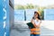 Smiling portrait of beautiful asian female industrial engineer wearing white helmet, vest holding walkie talkie. Safety Supervisor