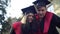 Smiling positive couple in graduation togas talking pointing looking at camera. Portrait of curios Caucasian young man