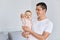 Smiling positive man holding his newborn baby daughter, man expressing happiness, spending time with hid child, posing indoor at