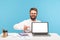 Smiling positive man office worker with beard pointing finger at laptop with empty screen, showing how to create website,