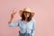 Smiling positive woman with dark hair shows peace gesture, happy to support idea, sends good vibes, wears straw hat