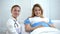 Smiling pregnant woman and gynecologist looking at camera, maternity hospital ad