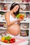 Smiling pregnant woman with a plate of fresh vegetable salad.