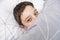 Smiling preteen boy child lying in bed and covering his tricky playful face with a blanket, pranking kid concept