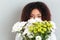 Smiling pretty african woman hiding behind flower bouquet