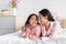 Smiling pretty cute korean millennial woman hugging teenage daughter in pink pajama lie on bed in bedroom