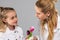 Smiling pretty girl in white jacket gifting flowers to her light-haired sister