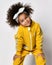 Smiling pretty small curly mulatto african girl in warm yellow jumpsuit and hair bow posing