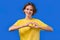 Smiling pretty woman showing sign of shape heart. Positive lady on blue background. Women health, volunteering, charity