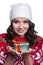Smiling pretty young woman wearing colorful knitted sweater with christmas ornament and hat, holding christmas gift.