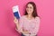 Smiling pretty young woman in white casual cshirt with red stripes holding passport, boarding pass tickets, happy passenger ready