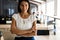 Smiling professional businesswoman in casual, with arms crossed standing in office.