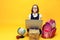 Smiling pupil sits behind a stack of books and laptop with globe looks at the camera Kids education