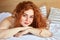 Smiling red haired female enjoy weekends lying on bed