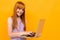 Smiling red-haired girl chatting on a laptop on a yellow banner background