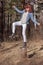 Smiling red-haired teen girl fooling around standing on one leg on a stump in the forest.