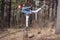 A smiling red-haired teenager girl does an acrobatic stunt called swallow on a stump in the forest.