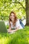 Smiling redhead using laptop in the park