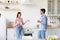 Smiling relaxed millennial caucasian woman and man with cups of drink talk on kitchen interior