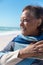 Smiling retired african american senior woman wrapped in shawl at beach on sunny day