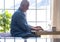 Smiling retired senior man with beard working with laptop at home. One modern elderly people using wireless technology drinking a