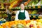 Smiling salesgirl in apron standing in fruit and vegetable store