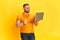 Smiling salesman holding laptop and working with pleasure over yellow background