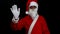 Smiling Santa Claus on black background raises his arm and greets with his hand.