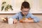 A smiling school-age boy sits at a table and brings fruits to him. With the other hand, he moves the sweets away from him.