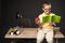 smiling school boy with apple doing homework and sitting on table with books lamp plant and  colour pencils on grey