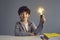 Smiling school boy child with light bulb sitting at desk against studio wall