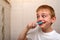 Smiling schoolboy diligently brushes his teeth in the bathroom. Healthy habits