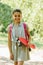 Smiling schoolgirl holding skateboard and looking at camera in park