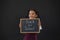 Smiling schoolgirl holding slate with text against blackboard