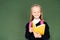 smiling schoolgirl reading book while standing near green chalkboard.