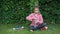 Smiling schoolgirl sits in the park on the grass and drinks water from a bottle. Child girl in a shirt is resting in the