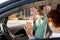 Smiling schoolgirl waving hand to her mom while getting out of car