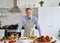 Smiling senior 50s man wearing apron standing in kitchen table preparing salad.