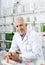 Smiling Senior Chemist Leaning On Counter In Pharmacy