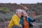 Smiling senior couple enjoying outdoors excursion at sunset light, using mobile phone for a selfie