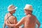 Smiling senior couple sitting on the edge of the swimming pool while looking into each other`s eyes. Two happy retirees enjoy