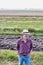 Smiling Senior farmer wearing hat, hands in pocket while standing in field