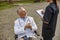 Smiling senior handicapped male doctor in wheelchair wearing lab coat having conversation with nurse making notes while