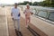 Smiling senior lady and man with bottles walk training together on city footbridge