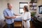 Smiling senior male patient and female therapist shaking hands against window