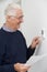 Smiling Senior Man With Bill Adjusting Central Heating Thermostat