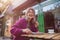 Smiling senior woman in knitted jacket eats tasty strawberry dessert at table in outdoors cafe