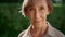 Smiling senior woman posing at camera in summer garden. Senior lady looking down